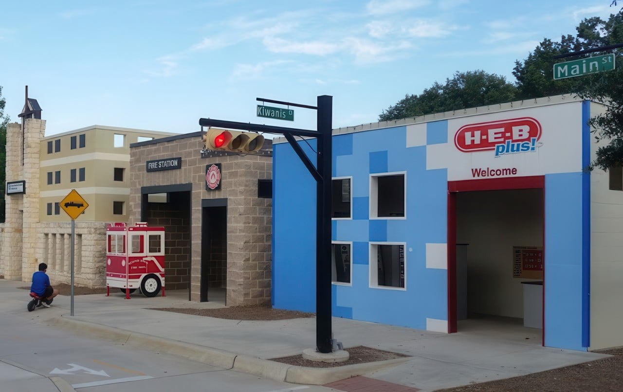 Play for All Park features a miniature cityscape with kid-sized buildings, traffic signals, a fire station, and play vehicles for immersive fun.