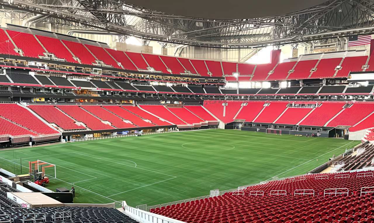 Wide view of Mercedes-Benz Stadium with vibrant green artificial turf and empty red seating, showcasing a pristine soccer field inside the modern domed arena in Atlanta.