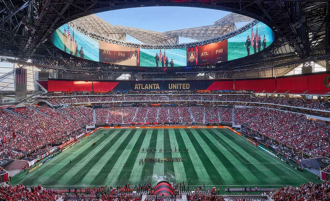 A packed Mercedes-Benz Stadium in Atlanta during an Atlanta United soccer match, featuring a lush green synthetic turf field, massive retractable roof, and large digital screens displaying pre-game ceremonies.
