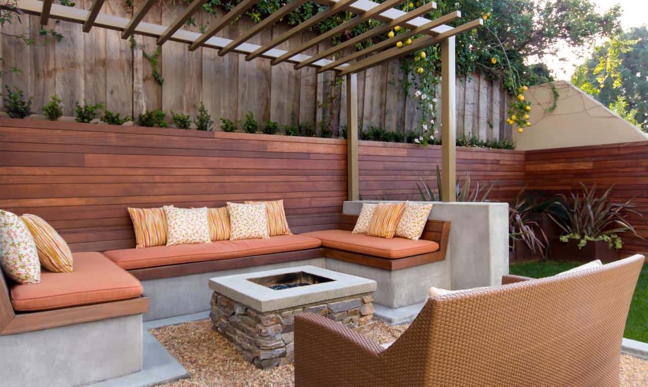 Cozy backyard firepit area with built-in wood and concrete bench seating, striped cushions, a stone fire feature, and pergola overhead.