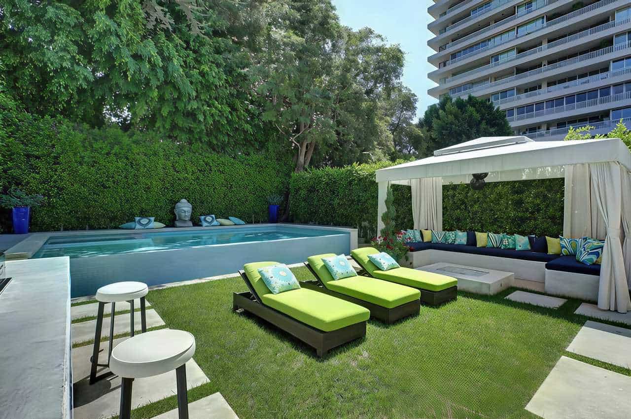 Apartment outdoor space with pool, cabana seating, lounge chairs, and turf landscaping framed by tall green hedges.