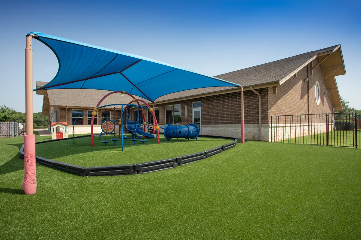 Artificial Turf Playground with play equipment and a sun sail outside a church